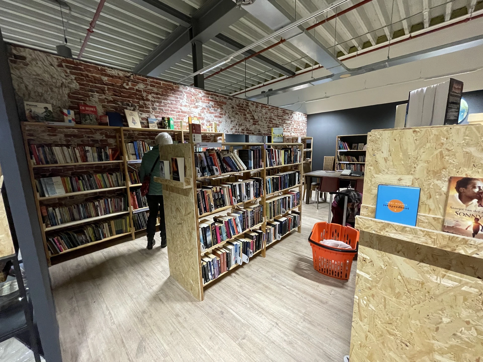 Boekenkasten met tweedehands boeken in een kringloopwinkel, met stellingen en oranje mand zichtbaar