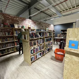 Boekenkasten met tweedehands boeken in een kringloopwinkel, met stellingen en oranje mand zichtbaar