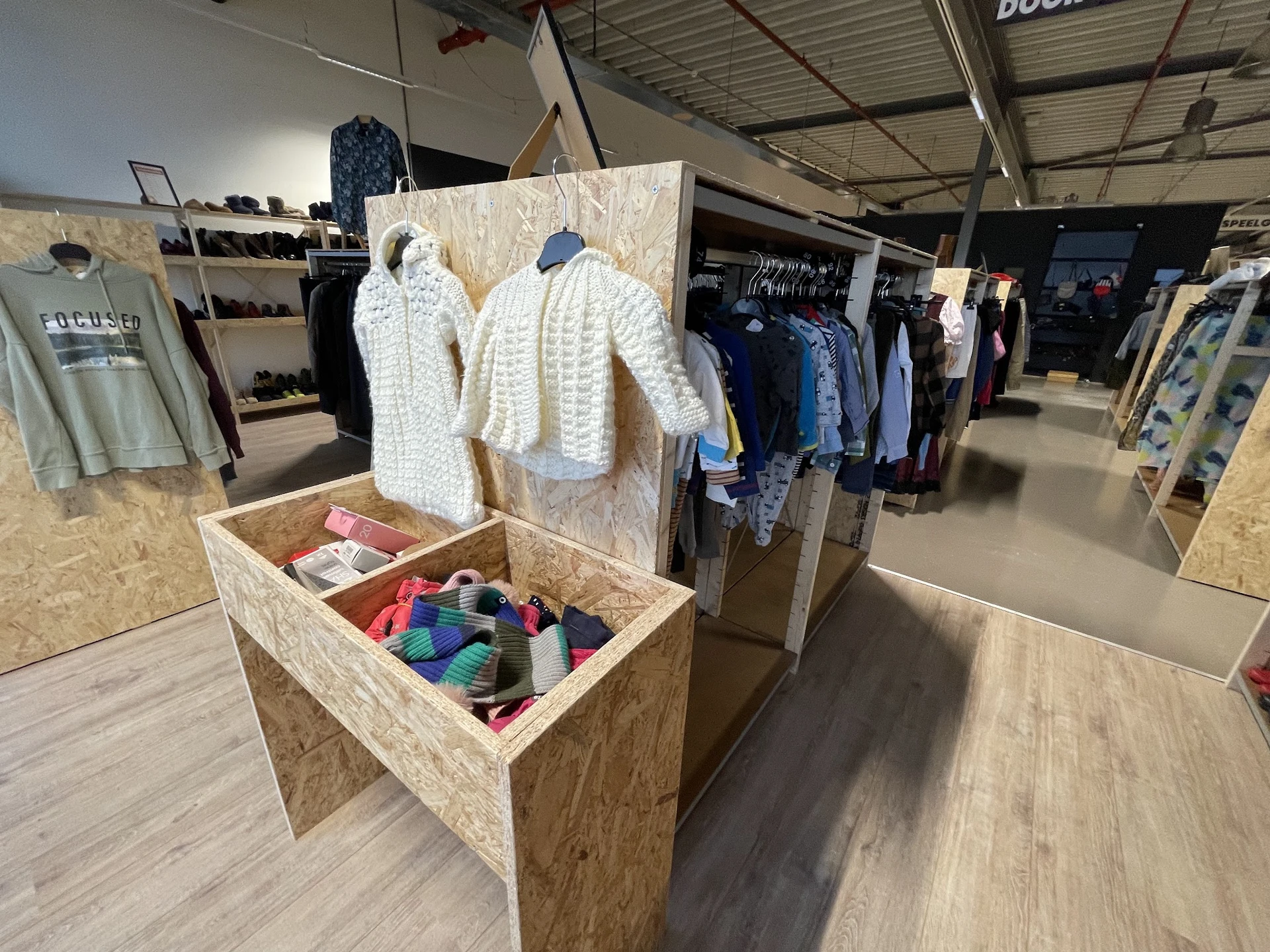 Kringloopwinkel display met gebreide kleding op hangers en kleurrijke textielspullen in een houten doos