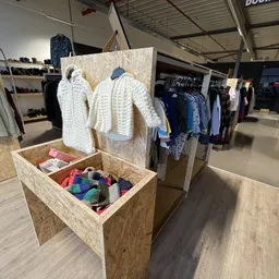 Kringloopwinkel display met gebreide kleding op hangers en kleurrijke textielspullen in een houten doos