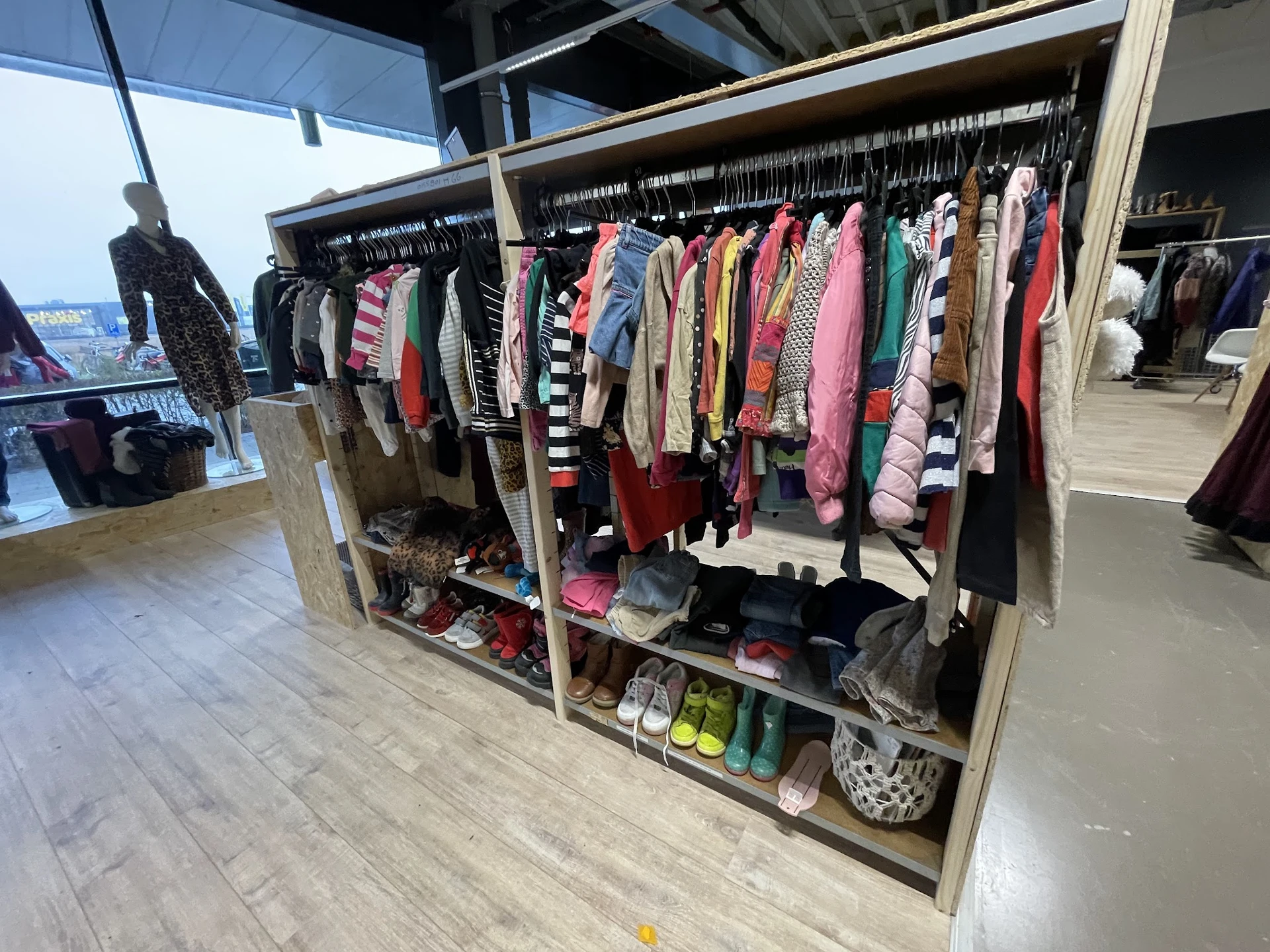 Rekken met kleding en schoenen in een kringloopwinkel, veelkleurige dames- en kinderkleding aan hangers
