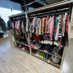 Rekken met kleding en schoenen in een kringloopwinkel, veelkleurige dames- en kinderkleding aan hangers