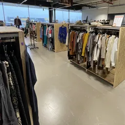 Winkelvloer met houten stellingen vol kleding aan hangers, grote ramen met uitzicht