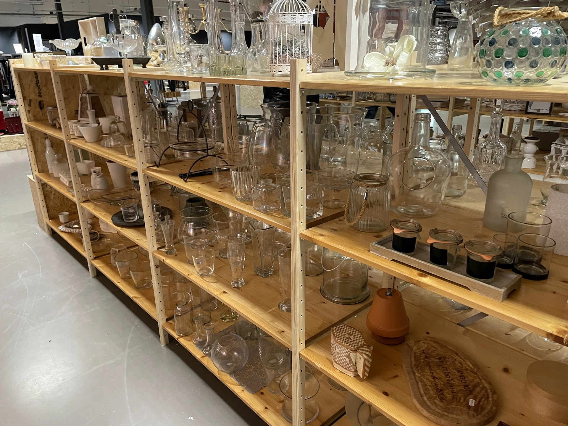 Houten stellingen vol met tweedehands glazen, potjes, vazen en huishoudartikel