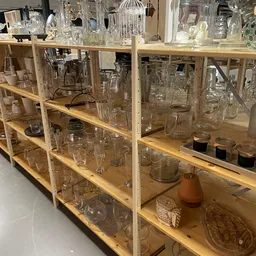 Houten stellingen vol met tweedehands glazen, potjes, vazen en huishoudartikel