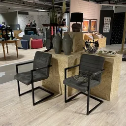 Tweedehands meubelen: zwarte stoelen met metalen frame rond gele/bruine kubusvormige elementen, met decoratieve items erop