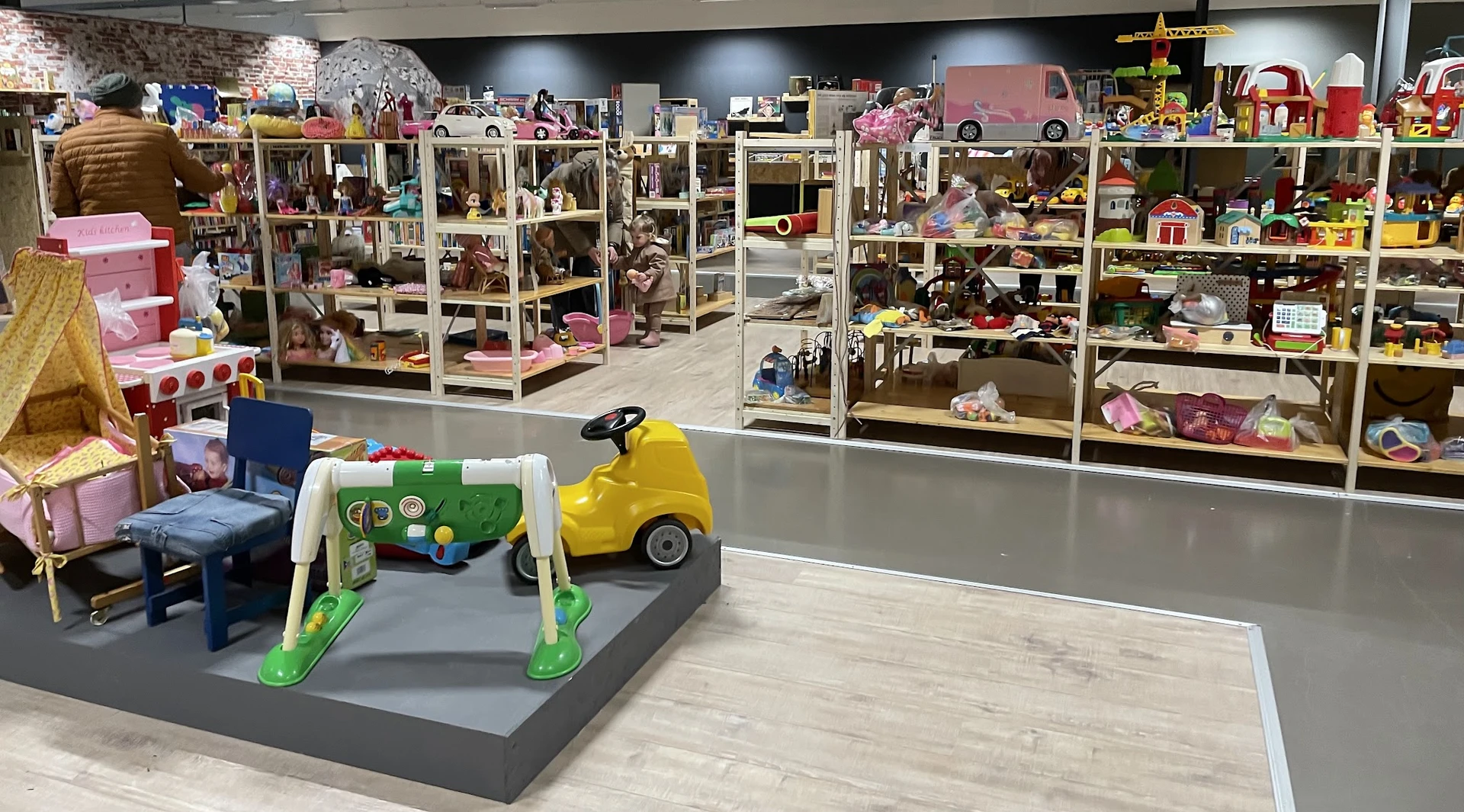 Speelgoedafdeling met speelgoedhuizen in vitrines en gele speelgoedauto op grijze sokkel
