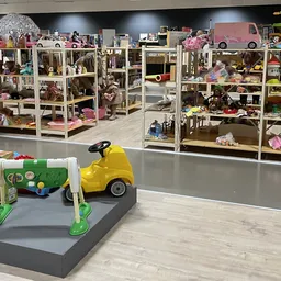 Speelgoedafdeling met speelgoedhuizen in vitrines en gele speelgoedauto op grijze sokkel