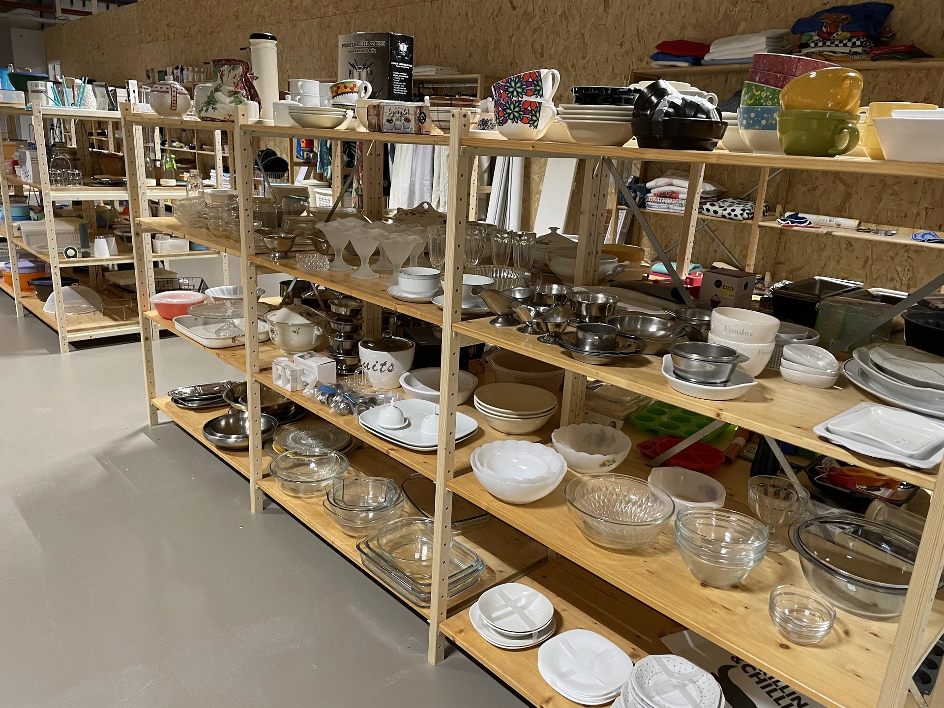 Houten stellingen met uitgestalde servies, glazen en keukenartikelen in een kringloopwinkel