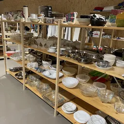 Houten stellingen met uitgestalde servies, glazen en keukenartikelen in een kringloopwinkel