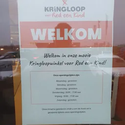 Welkomaffiche met openingstijden van de kringloopwinkel op een raam