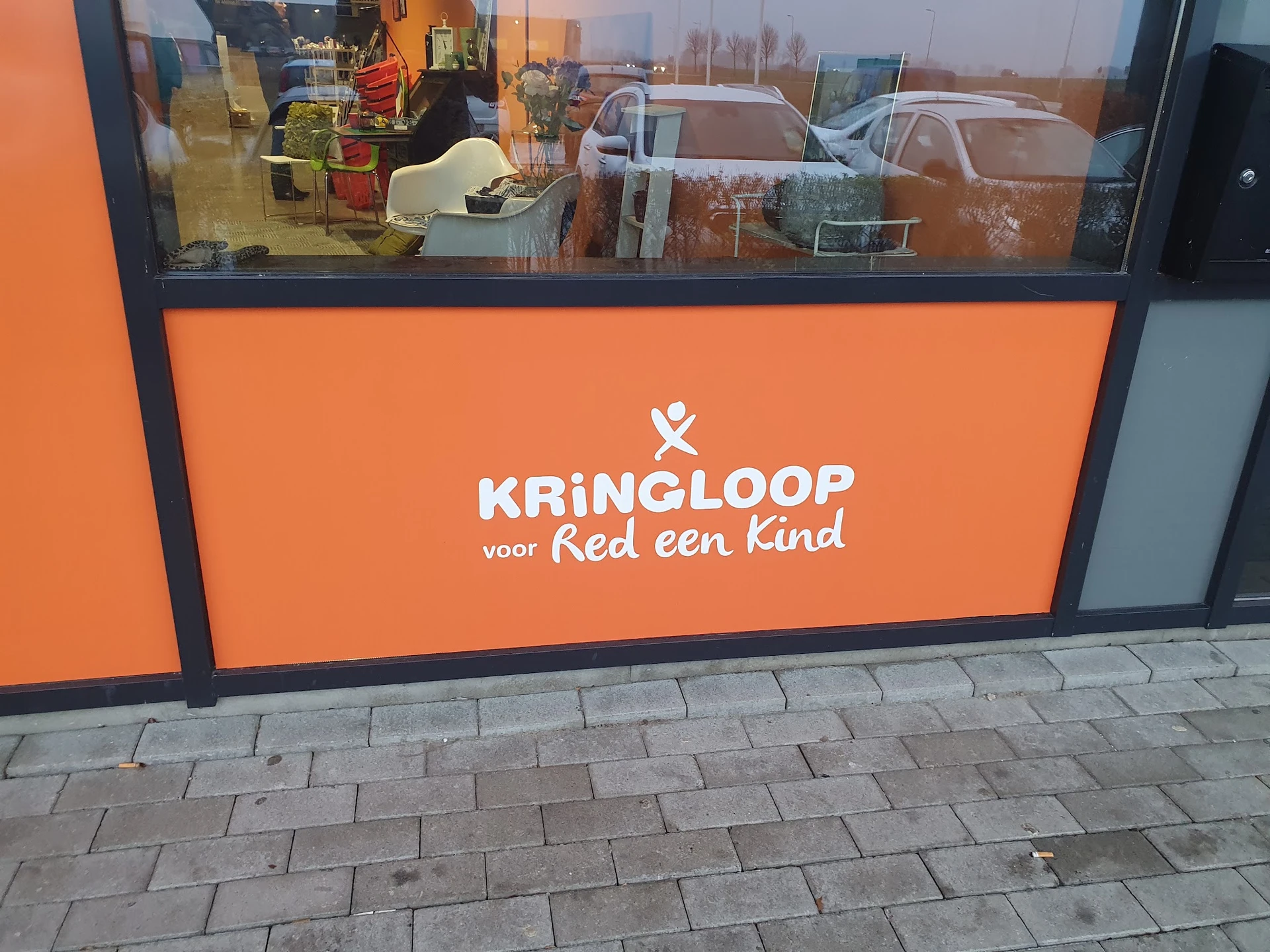Oranje gevel van kringloopwinkel met wit logo en tekst 'KRINGLOOP voor Red een Kind'