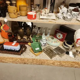 Verschillende huishoudelijke artikelen en serviesgoed uitgestald op tafels in een kringloopwinkel