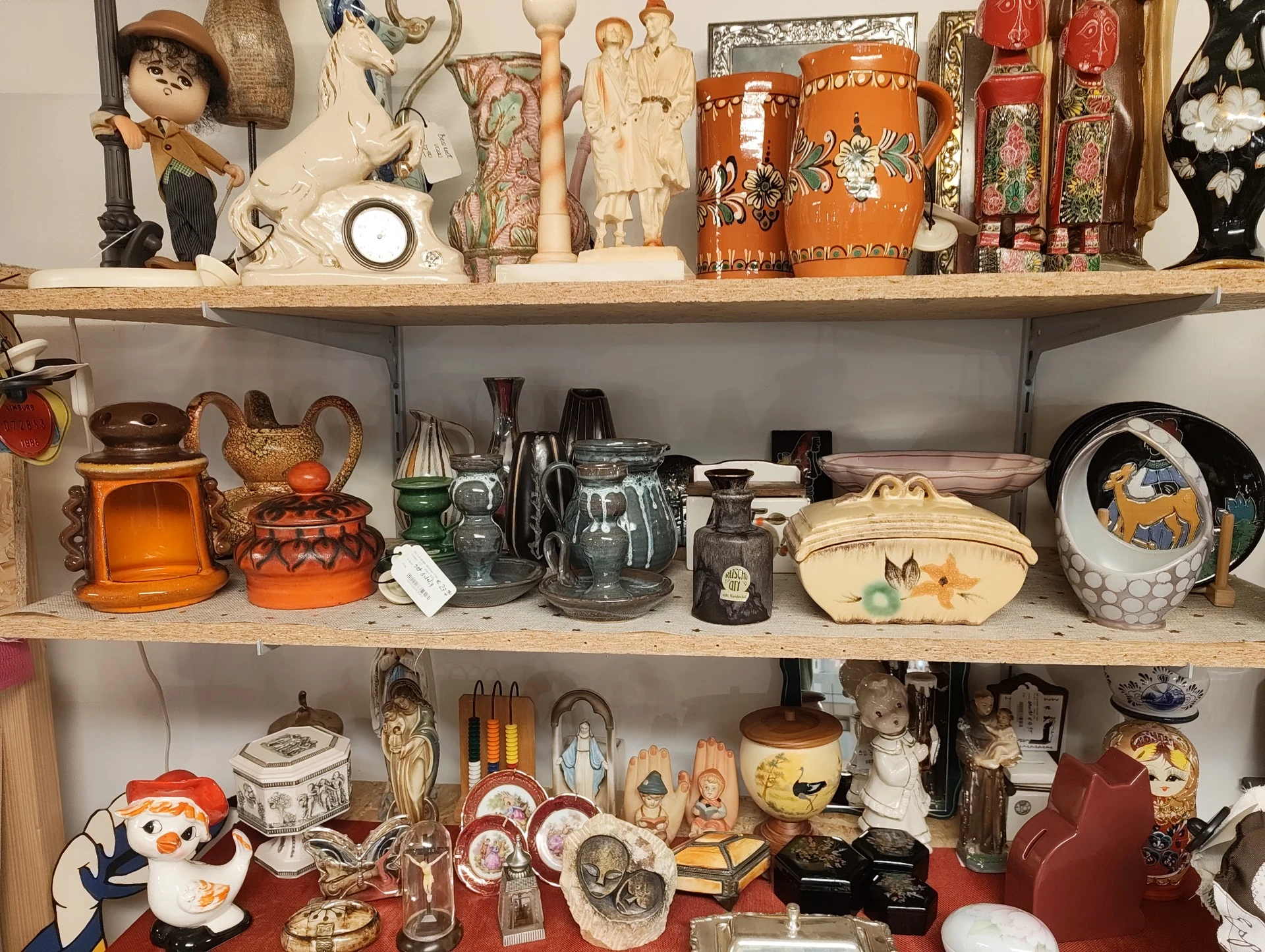 Drie volle schappen met verzamelde decoratieve artikelen: beeldjes, servies, vazen, kannen en kunstobjecten