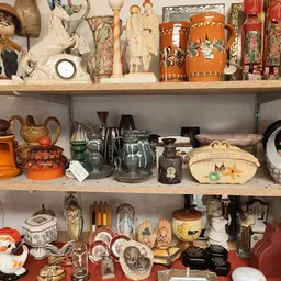 Drie volle schappen met verzamelde decoratieve artikelen: beeldjes, servies, vazen, kannen en kunstobjecten