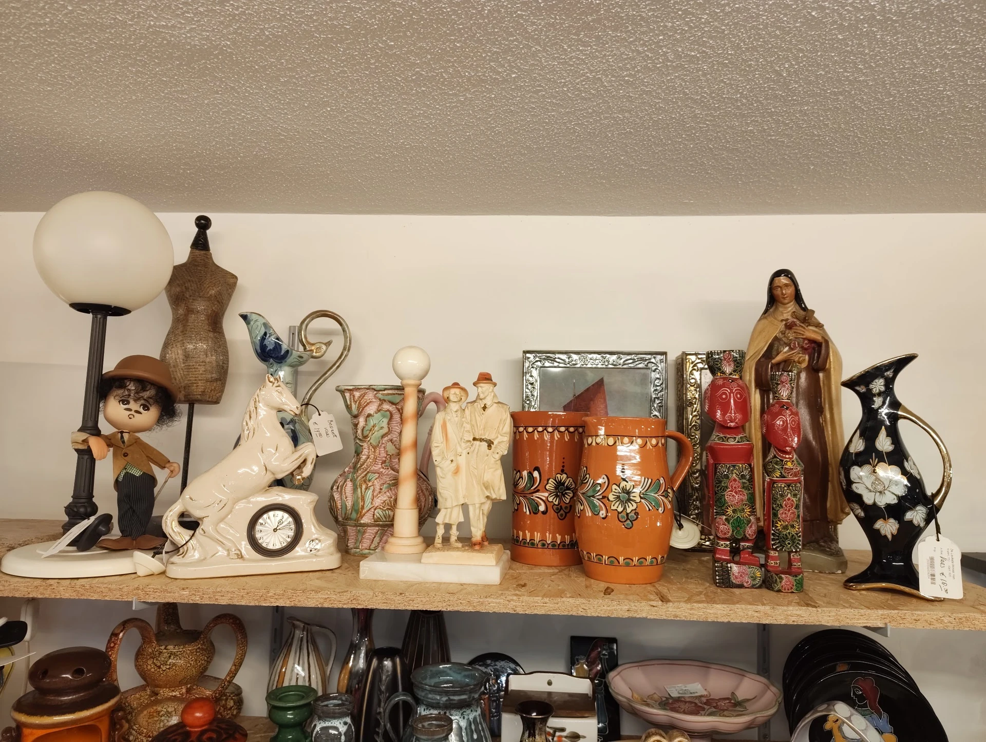 Schapplank met diverse decoratieve items: lampen, beelden, kandelaars en andere huishoudartikelen