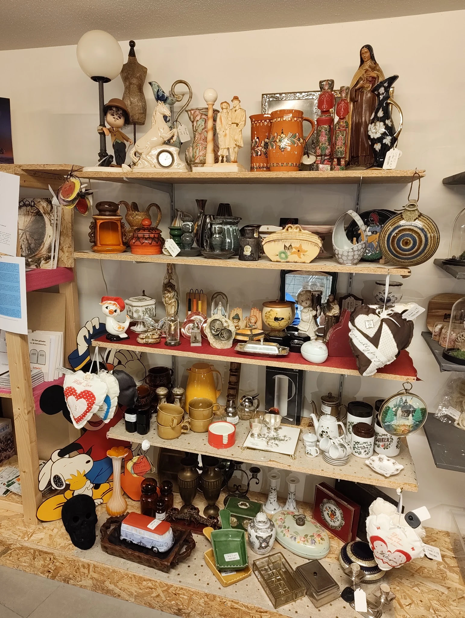 Houten wandplank met diverse tweedehands huishoudartikelen: servies, pannen, decoratieobjecten en keukenspullen