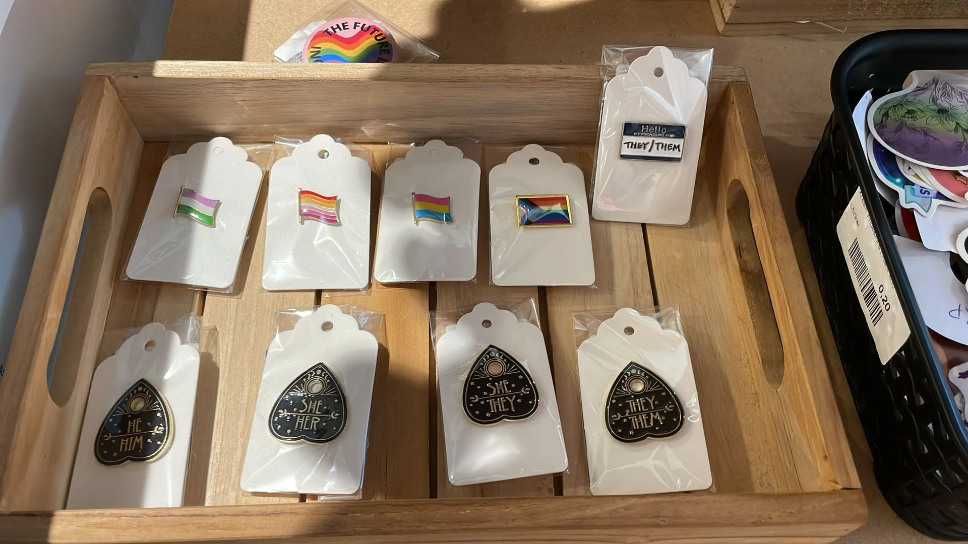 Uitgestalde items op houten planken: kaarten met regenboogvlaggen en zwarte hartvormige hangers met tekst