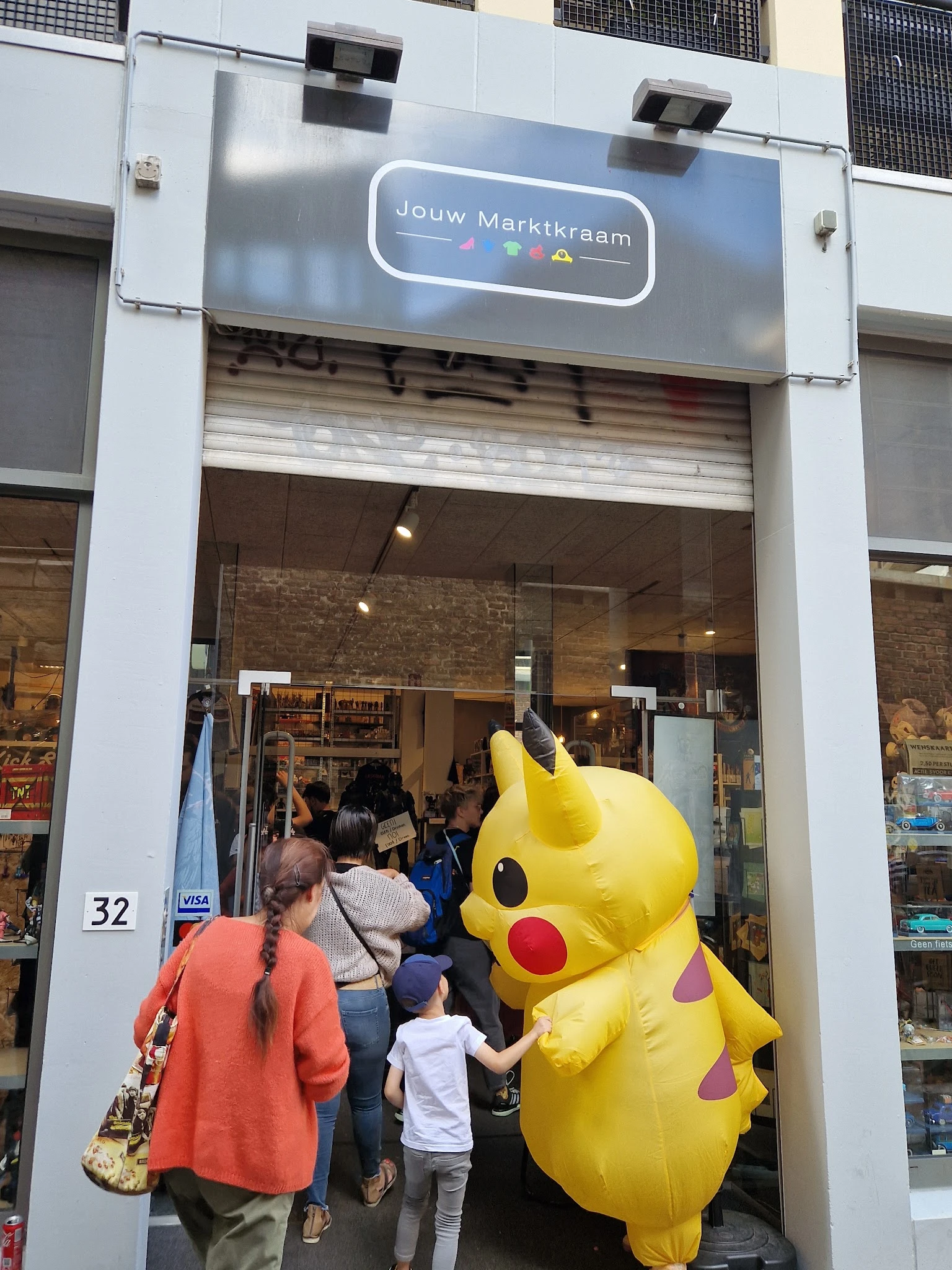Winkelpui met grote gele Pikachu-pop voor de ingang, bezoekers zichtbaar