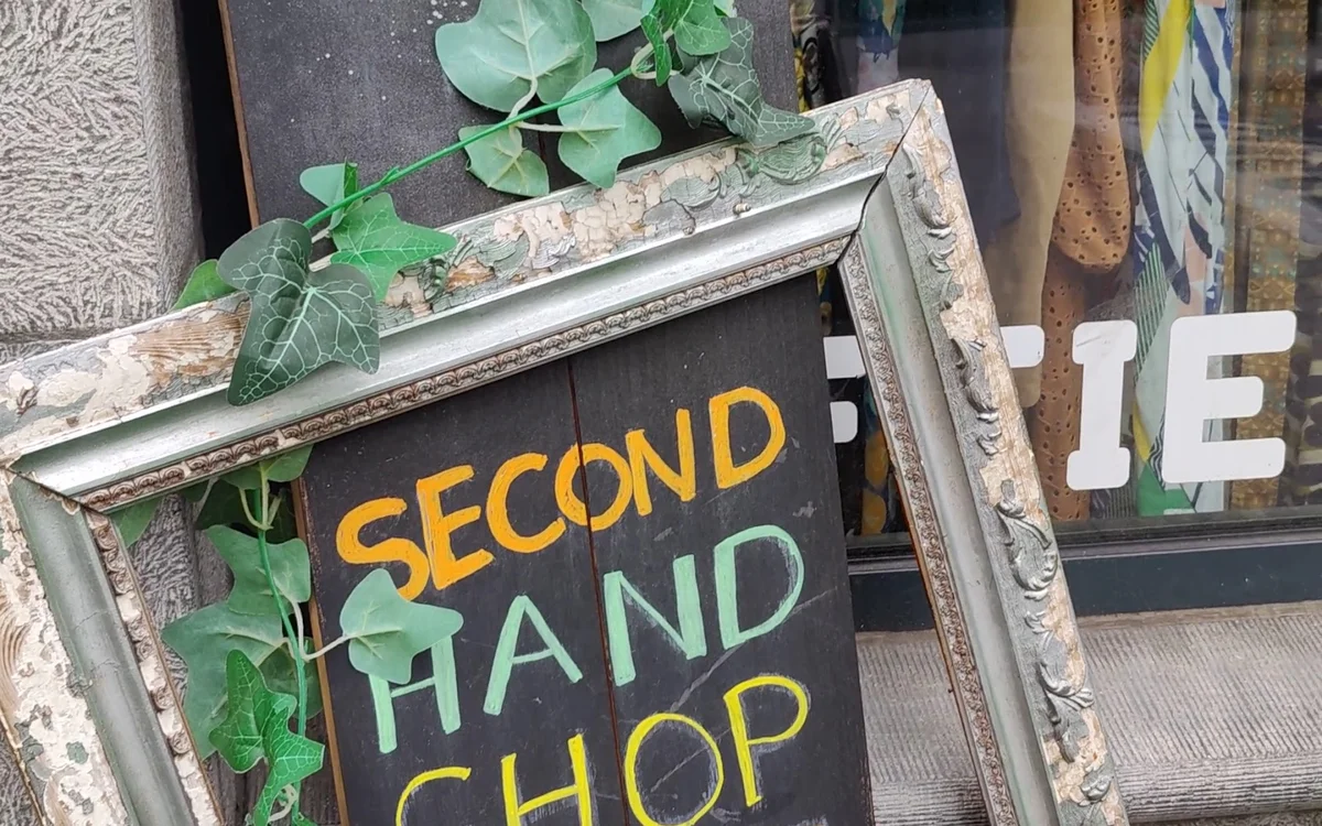 Winkelruit met krijtbord waarop 'SECOND HAND CHOP' in gele en groene letters, omgeven door groene klimop