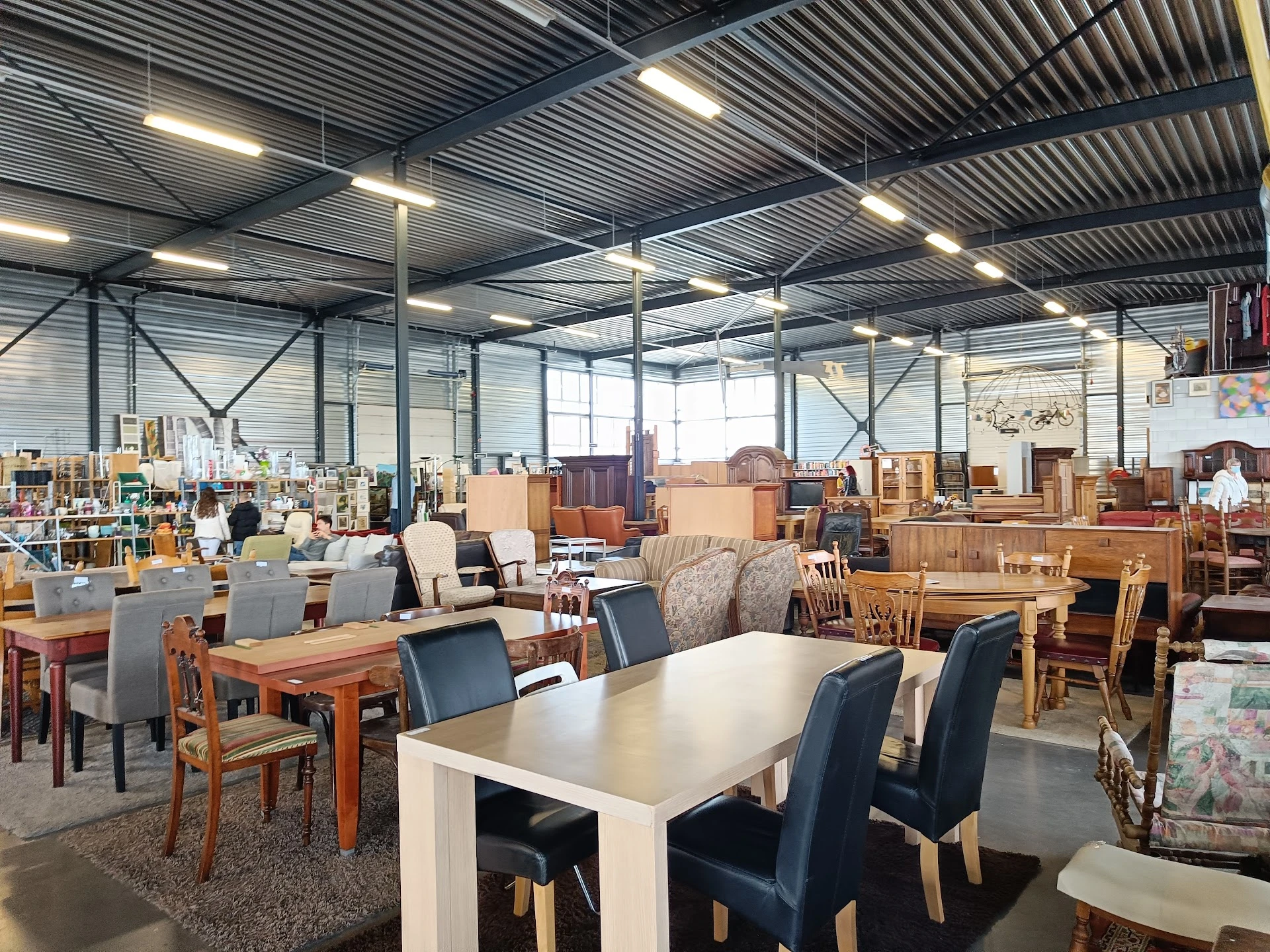 Ruime winkelhal met diverse meubels, tafels en stoelen uitgestald onder industriële plafondverlichting