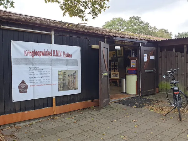Zwart houten pand met informatiebord en ingang, fiets ernaast, herfstbladeren op straat