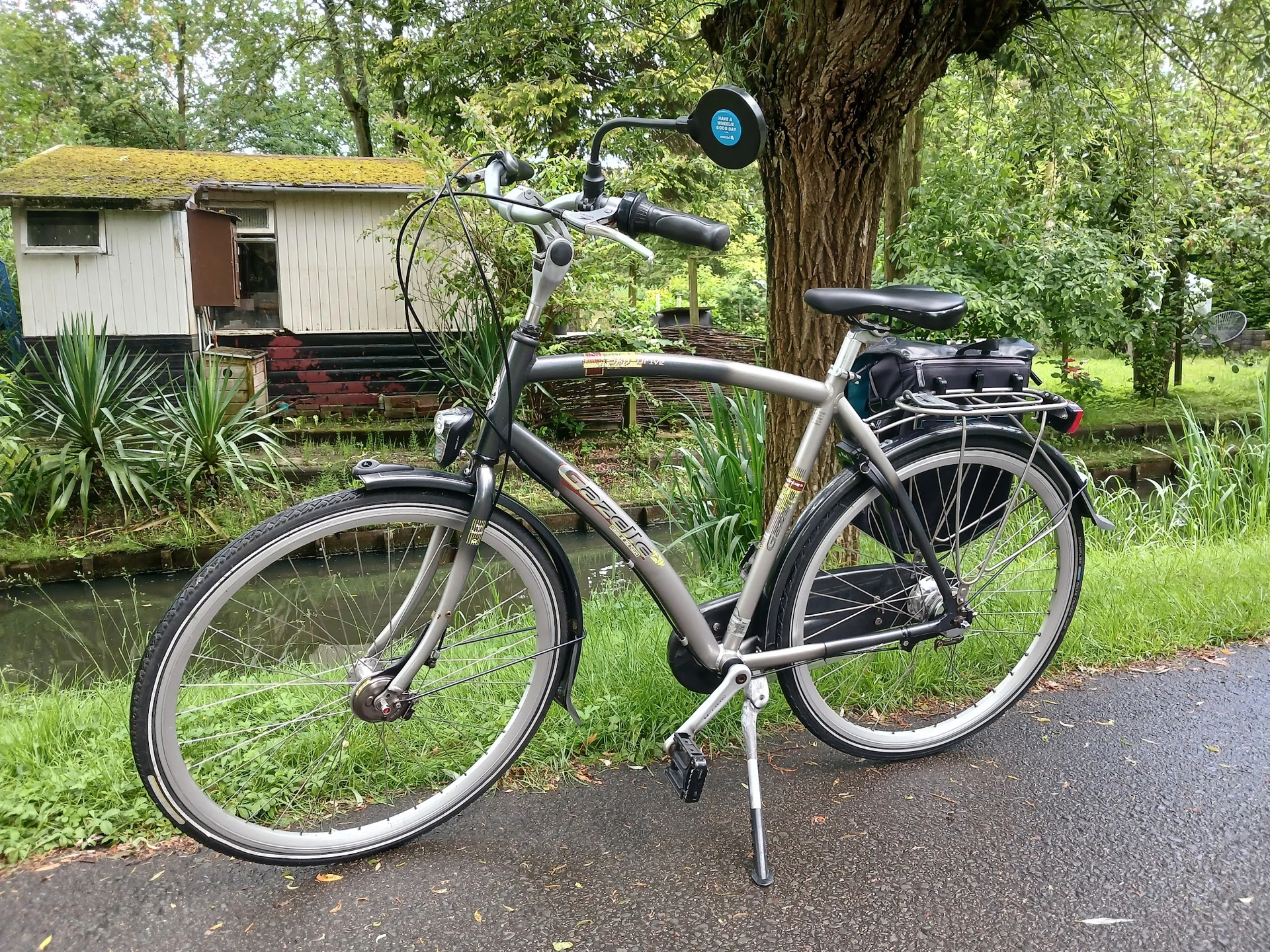 Zilverkleurige elektrische fiets met bagagedrager, tegen standaard geparkeerd op asfalt