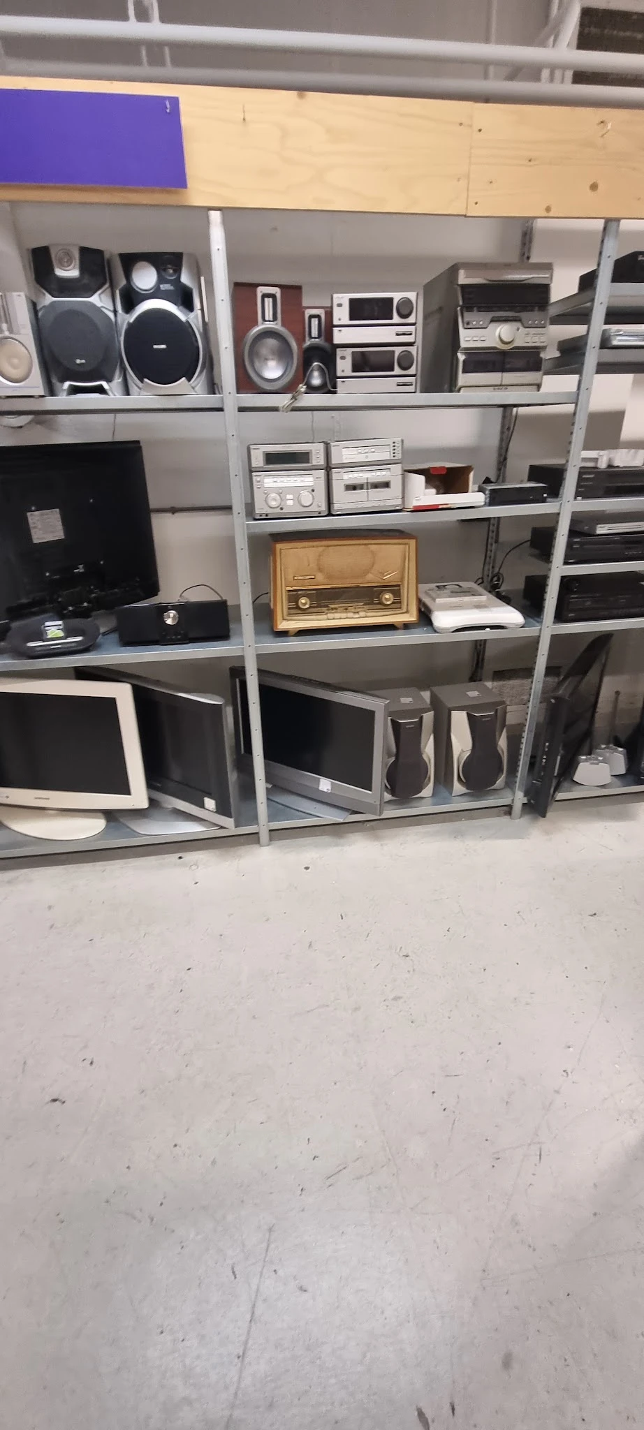 Stellingen met elektronische apparaten: monitoren, radio, speakers en kastjes in een kringloopwinkel