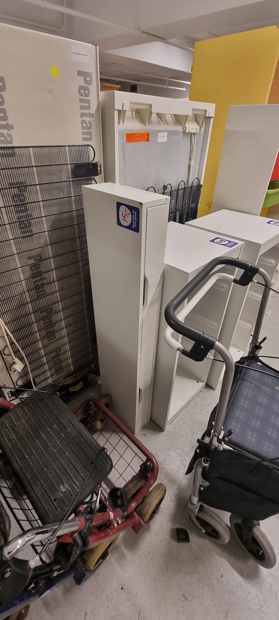 Tweedehands apparaten en huishoudelijke artikelen in de winkel, waaronder een ventilator, witte dozen en een hometrainer