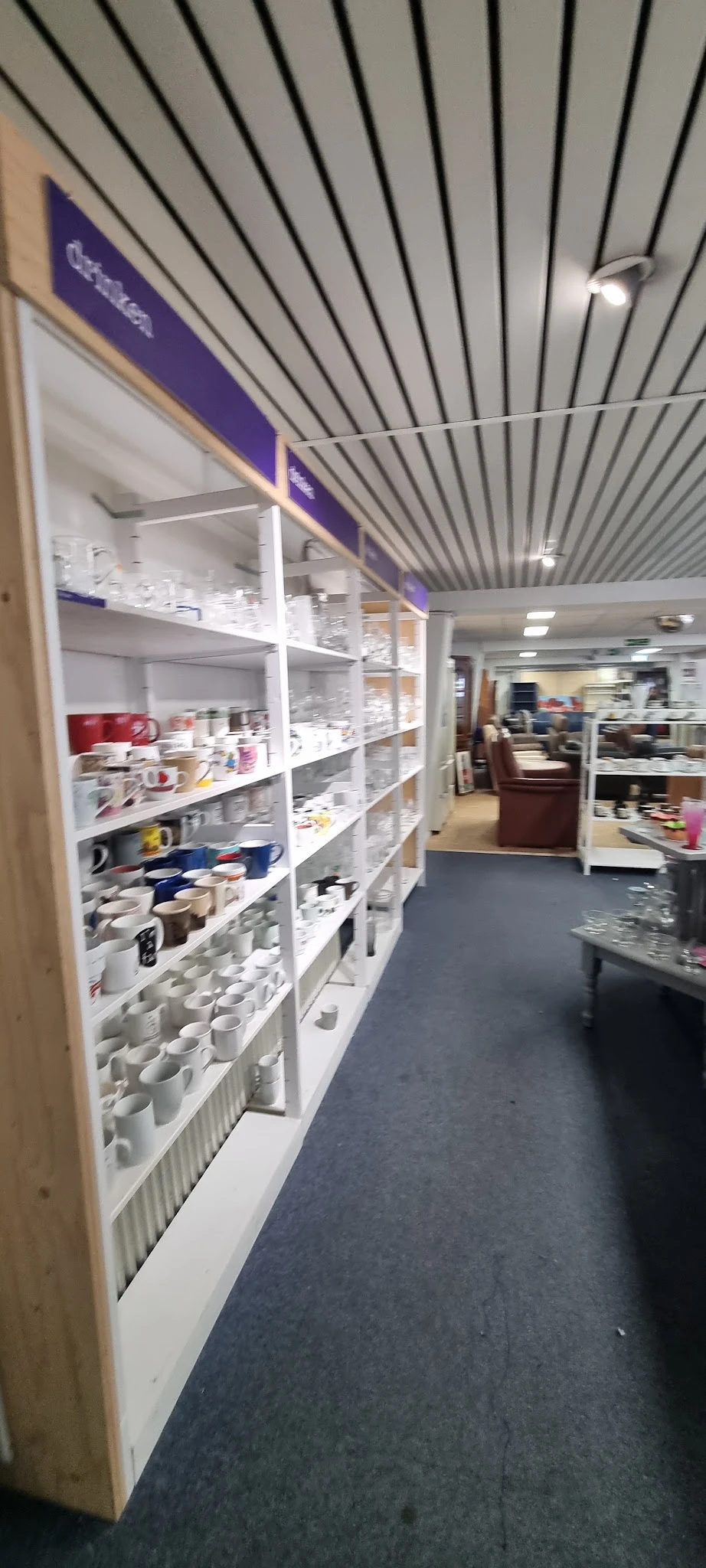 Witte stellingen met diverse huishoudelijke artikelen en servies in een kringloopwinkel
