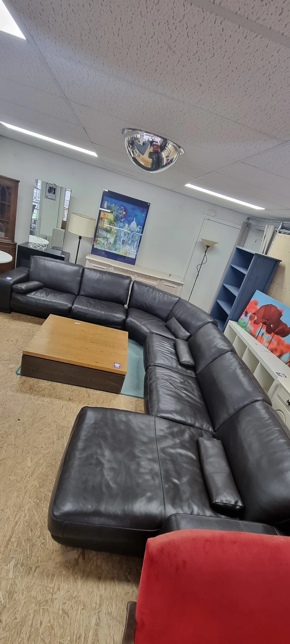Zithoek met grijze leren hoekbank, houten salontafel en stellingen met diverse spullen in een kringloopwinkel