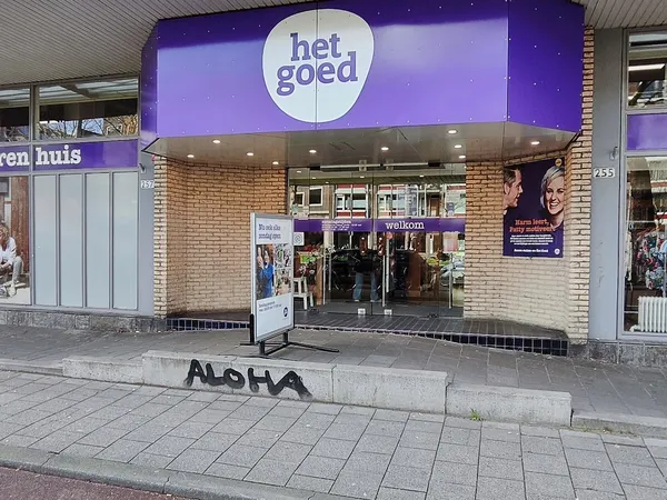 Gevel van kringloopwinkel 'het goed' met paarse uitbouw, glazen ingang en winkelnaam op verlicht bord