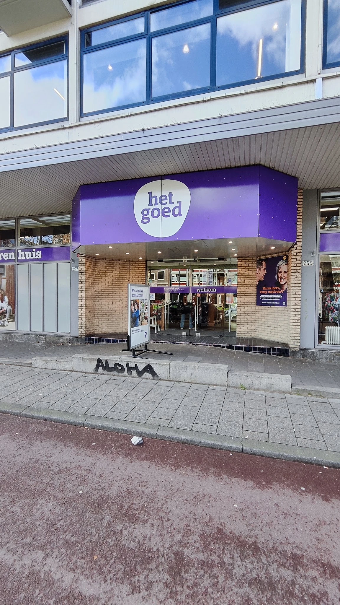 Gevel van kringloopwinkel 'het goed' met paarse uitbouw, glazen ingang en winkelnaam op verlicht bord