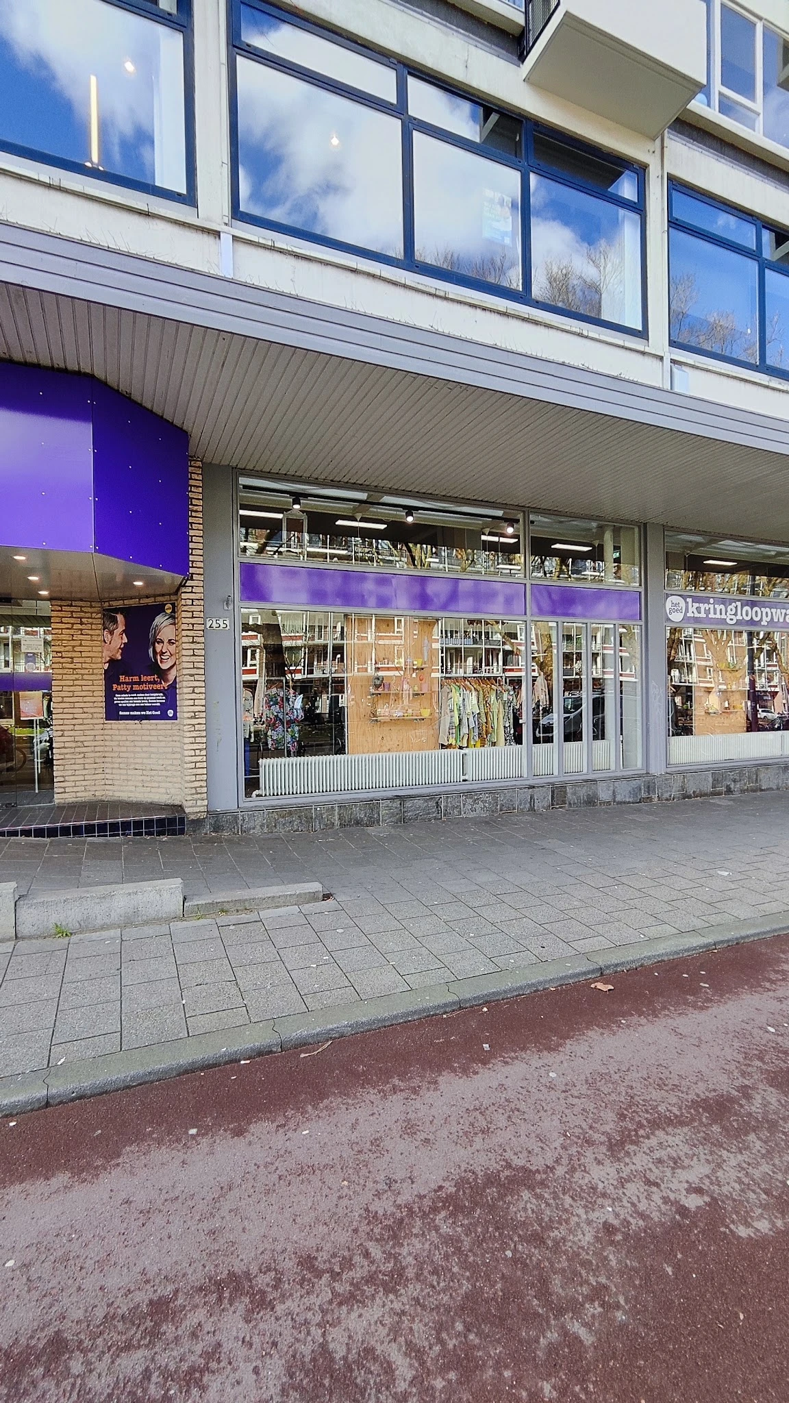 Winkelgevel met paarse banner, grote ramen met boekenrekken zichtbaar, bakstenen gevel en winkeluitstalling