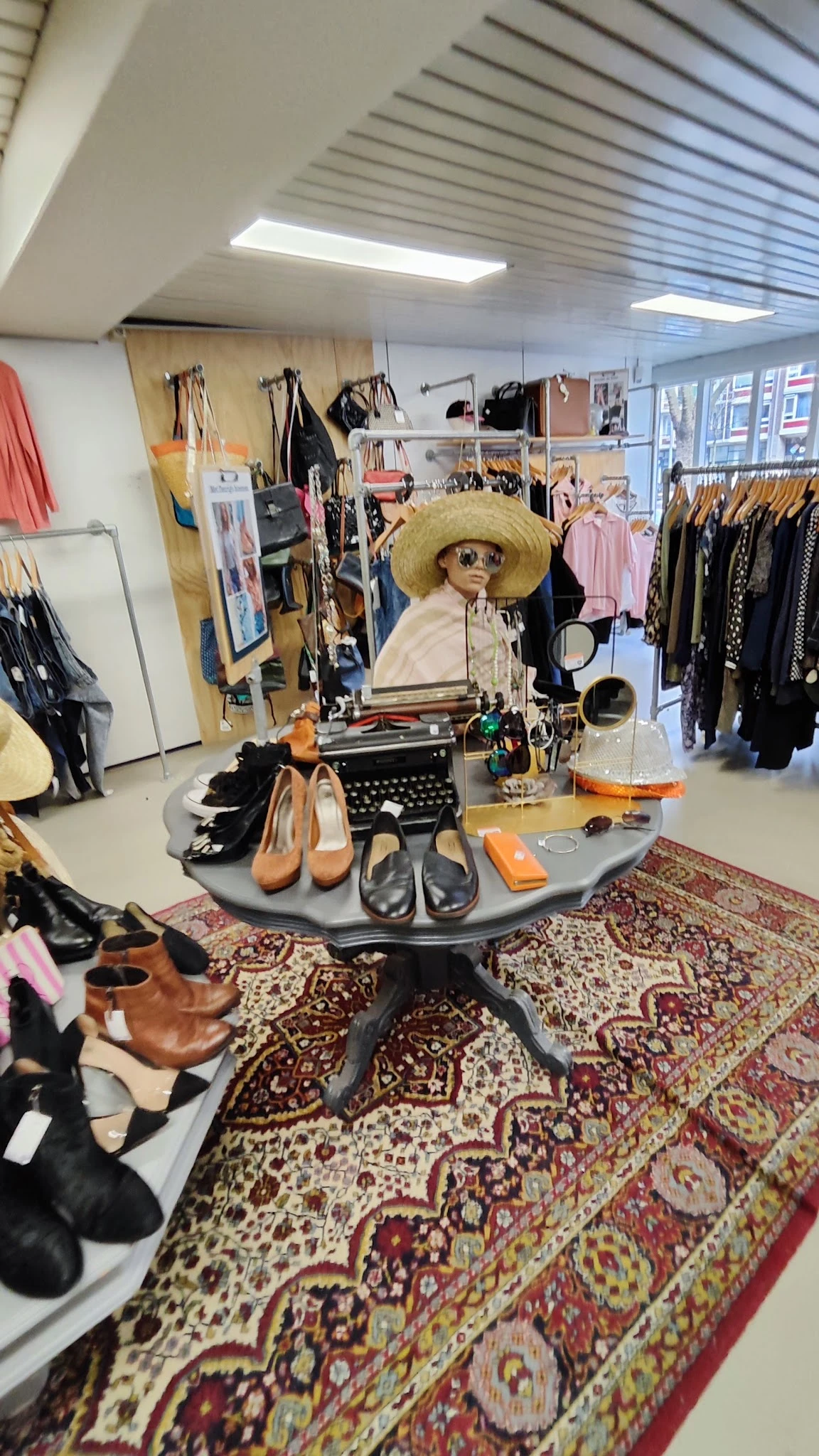 Winkelinterieur met kledingrekken en een creatieve display van schoenen, hoed en schrijfmachine op een tafel