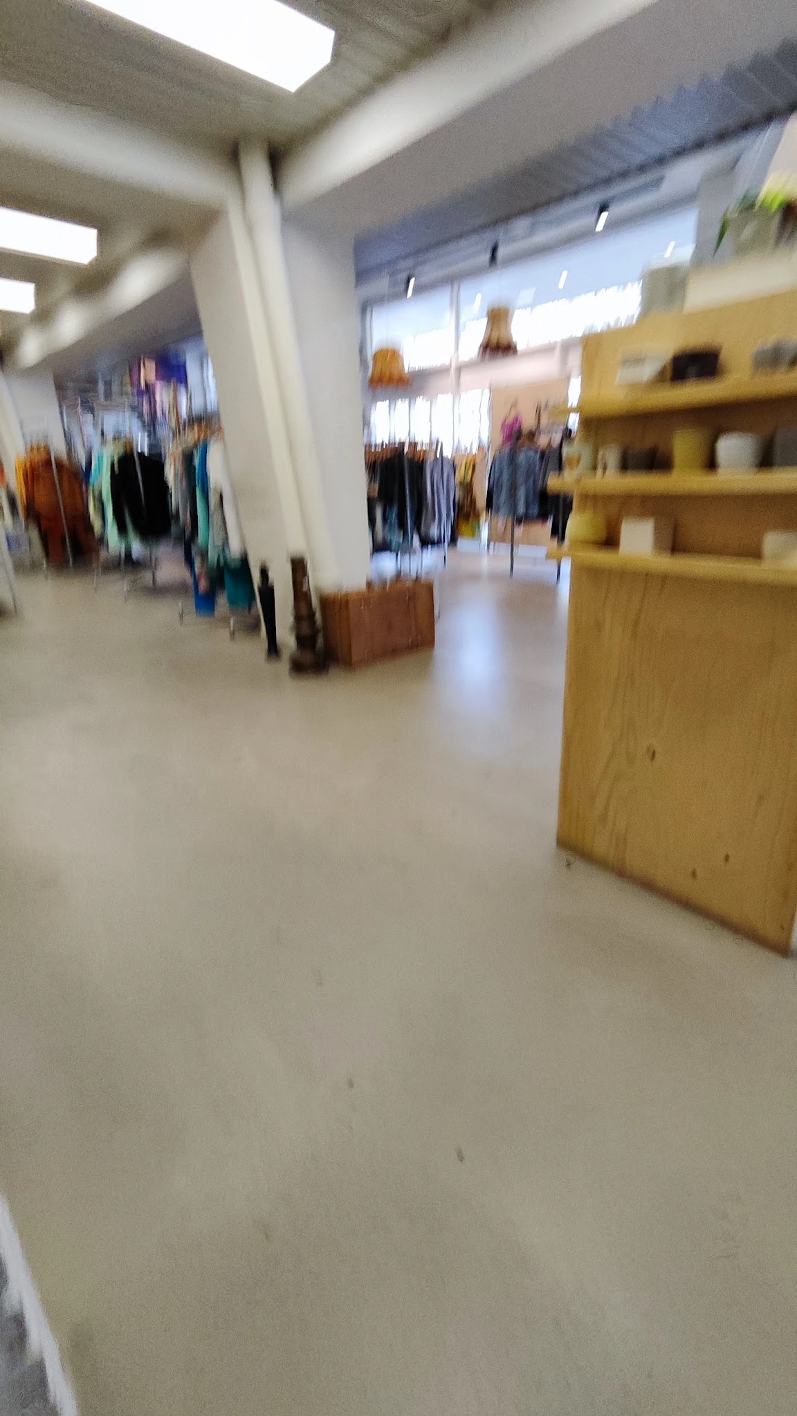 Winkelvloer van een kringloopwinkel met houten kasten en vage kledingrekken op de achtergrond