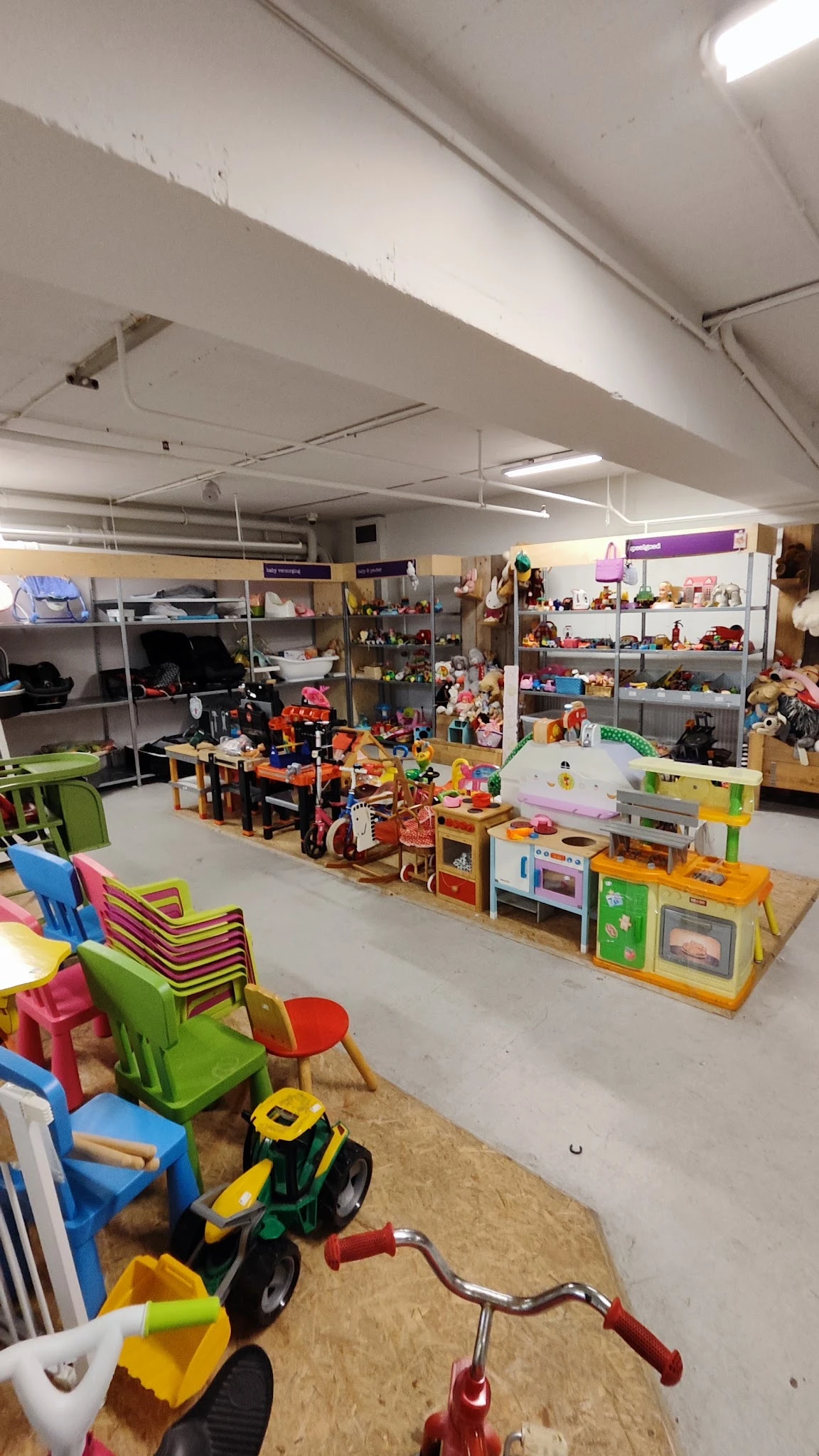 Speelgoedafdeling met gekleurde stoelen, speelkeukensets en speelgoed op stellingen