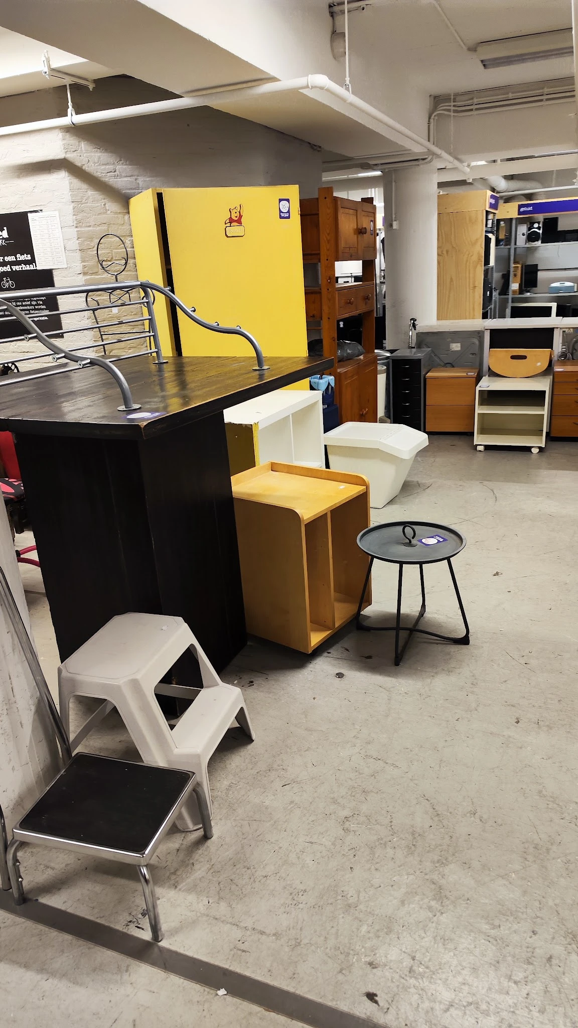 Winkelvloer met diverse meubelstukken: gele stoelen, zwarte tafel, witte opbergkisten en ronde bijzettafel