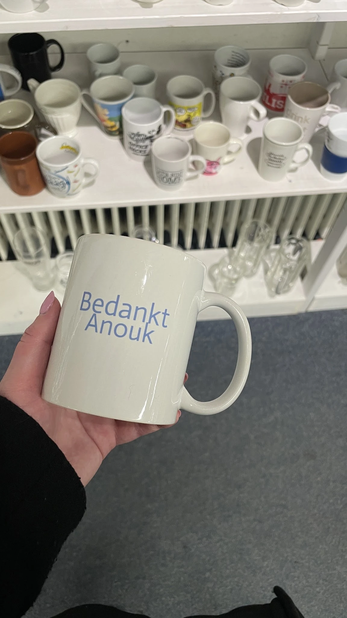 Witte mok met blauwe opdruk 'Bedankt Anouk' in iemands hand
