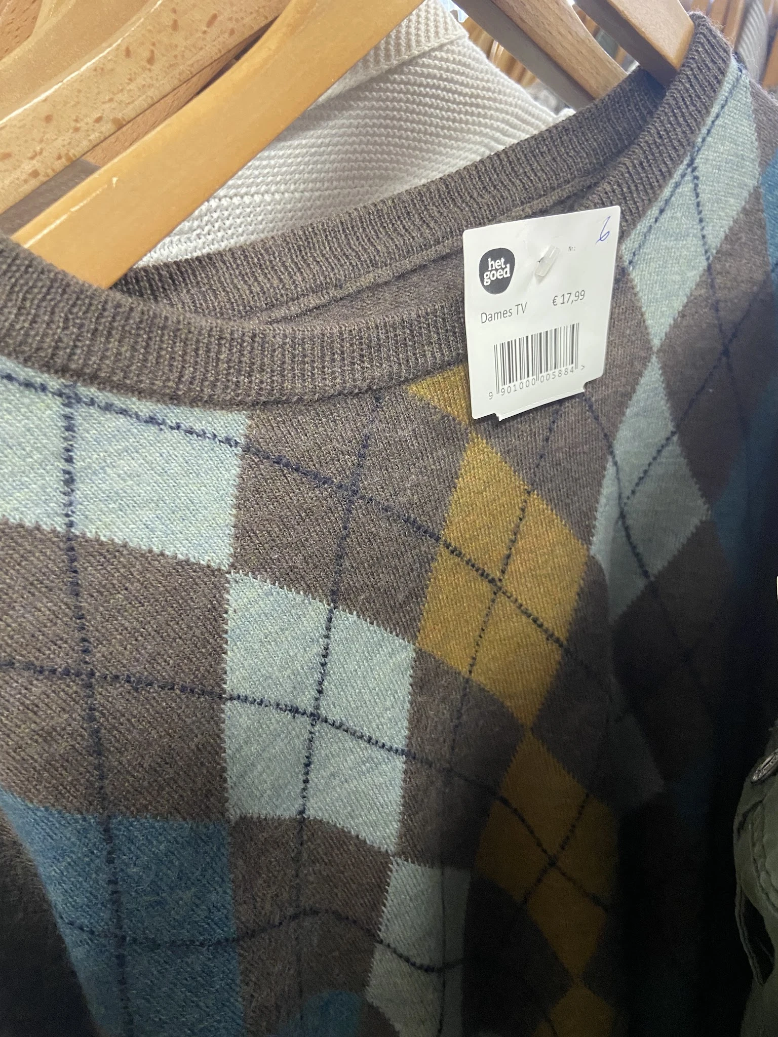 Close-up van een grijze trui met argyle-patroon in wit, geel en bruin, met prijskaartje