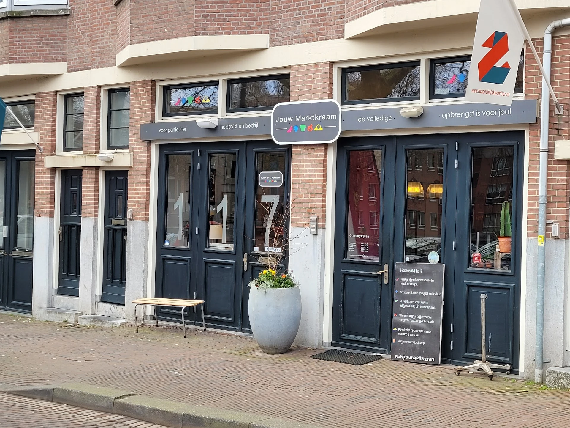 Donkerblauwe winkelpui van kringloopwinkel met ramen, deuren en aantal hangertjes buiten