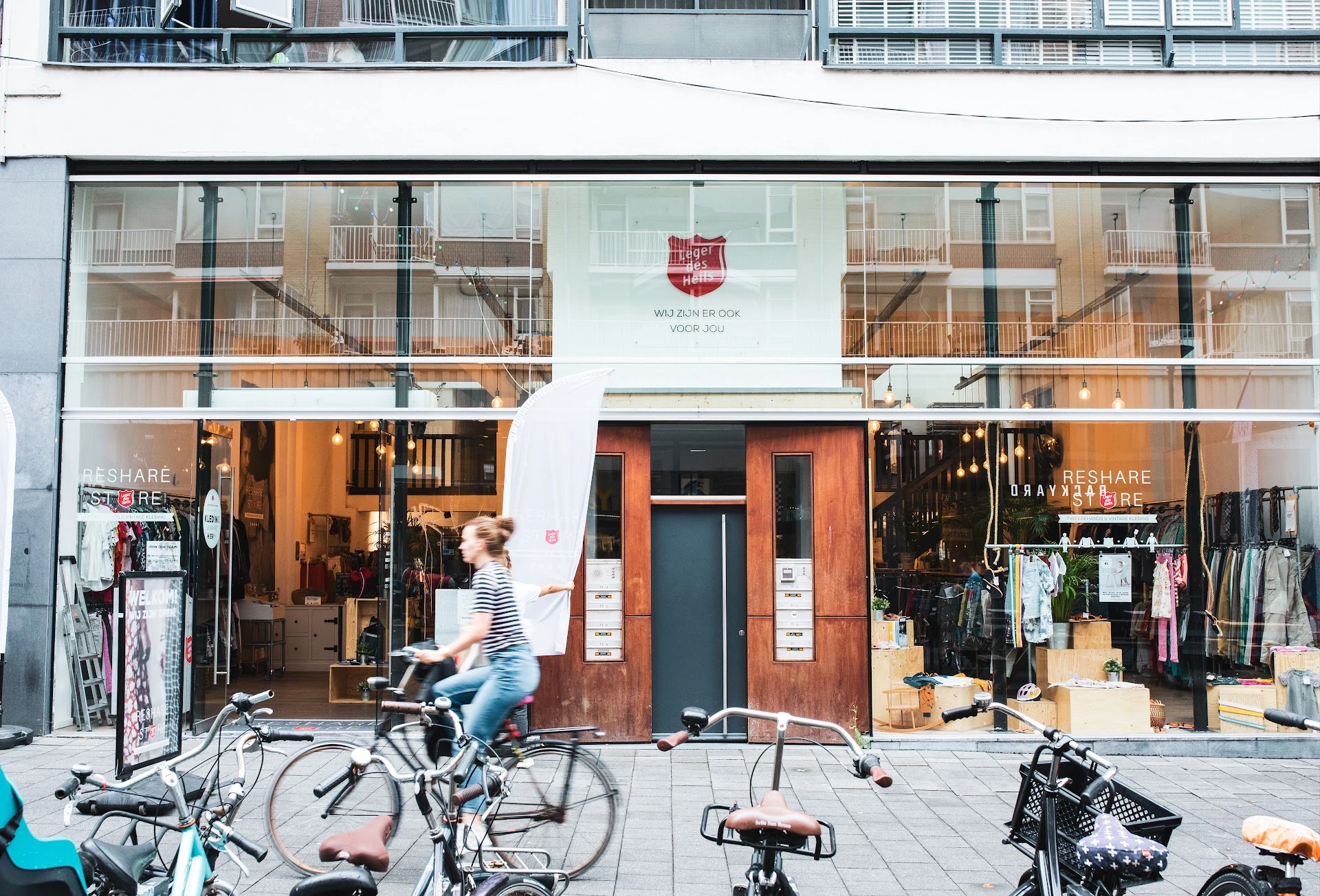 Winkelgevel met grote ramen, oranje deur in het midden, winkelnaam boven, fietsen op straat ervoor