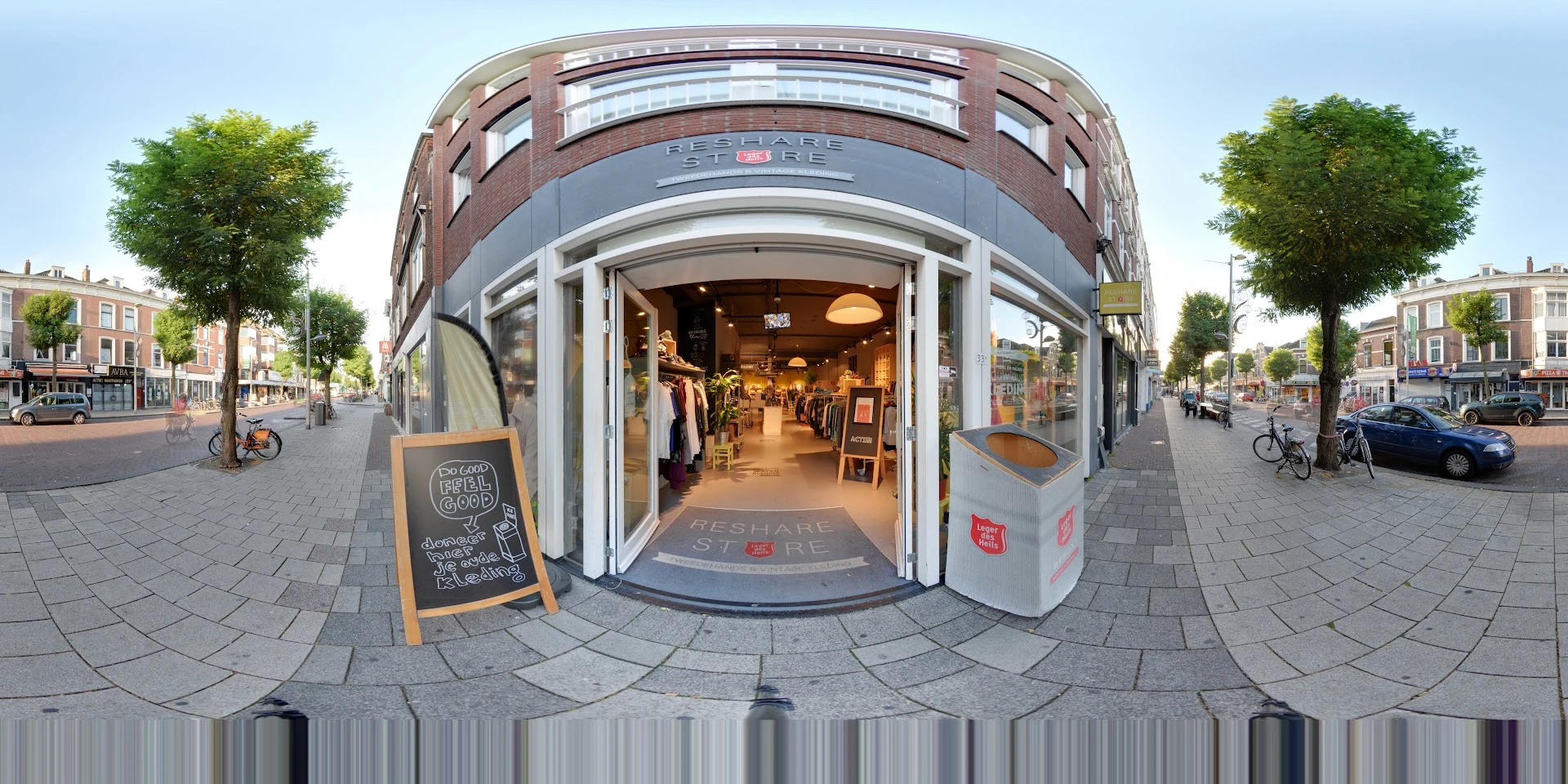 Hoekpand met grote ronde ramen en witte kozijnen aan een plein met straatstenen, groen zichtbaar aan zijkanten
