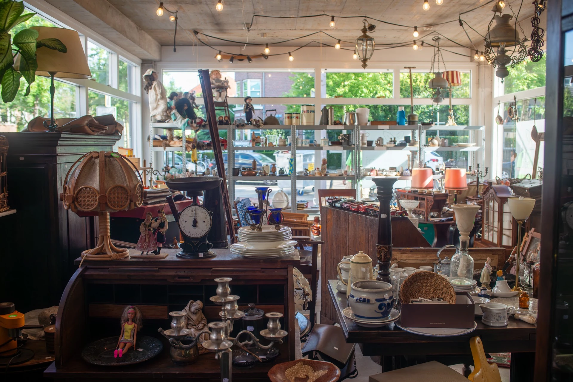Verzameling van tweedehands huishoudelijke spullen, servies, lampen en decoratieve items uitgestald op tafels en in vitrineka