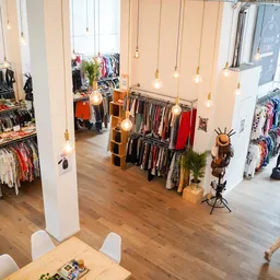 Ruim interieur van kringloopwinkel met kledingrekken, hangende lampen en houten vloer