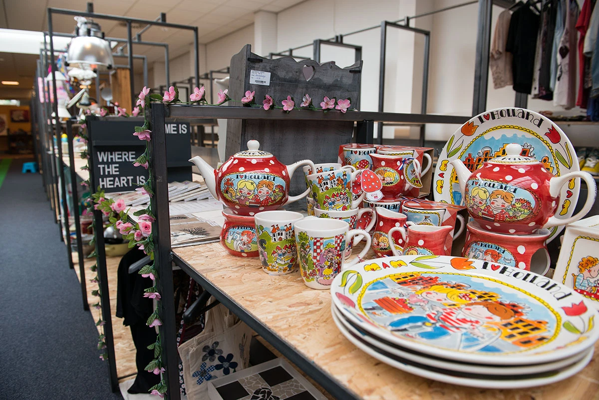 Uitgestalde serviesgoed met kleurrijke decoratieve borden, kopjes en theepotten op een houten tafel