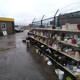Metalen stellingen buiten met diverse huishoudelijke artikelen en decoratieve items zoals vazen, kandelaars en potten