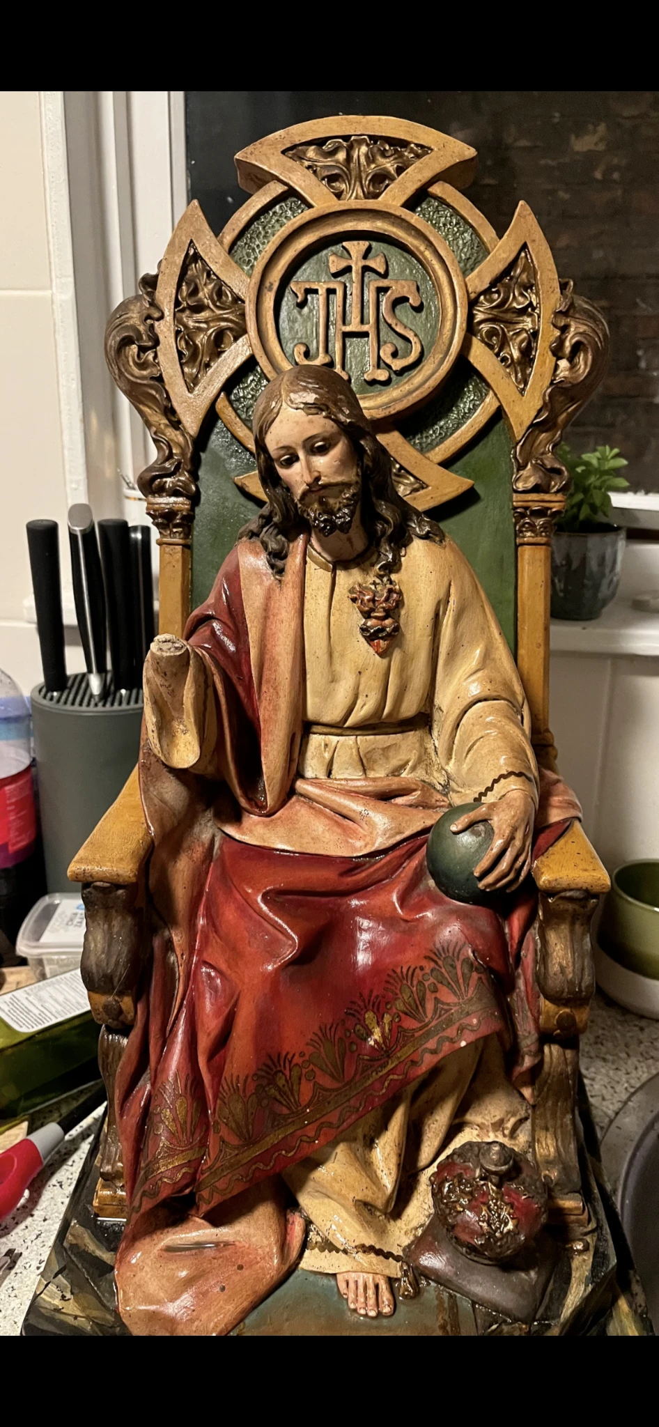 Houten beeldhouwwerk van Jezus zittend in rood en goudkleurig gewaad met kruis