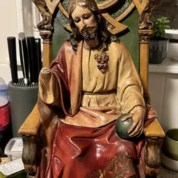 Houten beeldhouwwerk van Jezus zittend in rood en goudkleurig gewaad met kruis