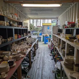 Binnenaanzicht van kringloopwinkel met stellingen vol serviesgoed, glazen en huishoudelijke artikelen langs beide zijden